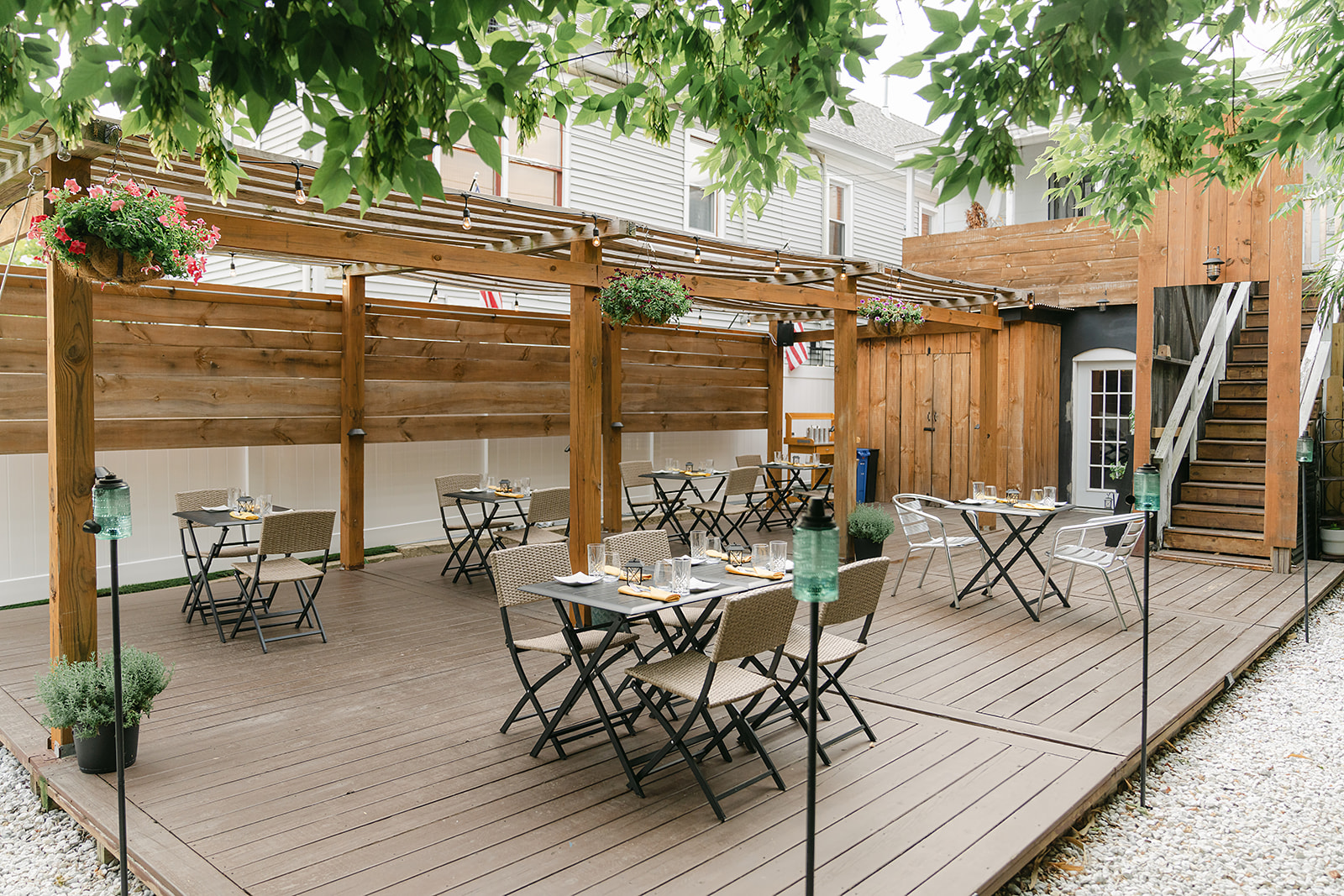 Petunia Patio Space. Tables and Chairs are set up for dining beneath a canopy of greenery and a wooden overhang.
